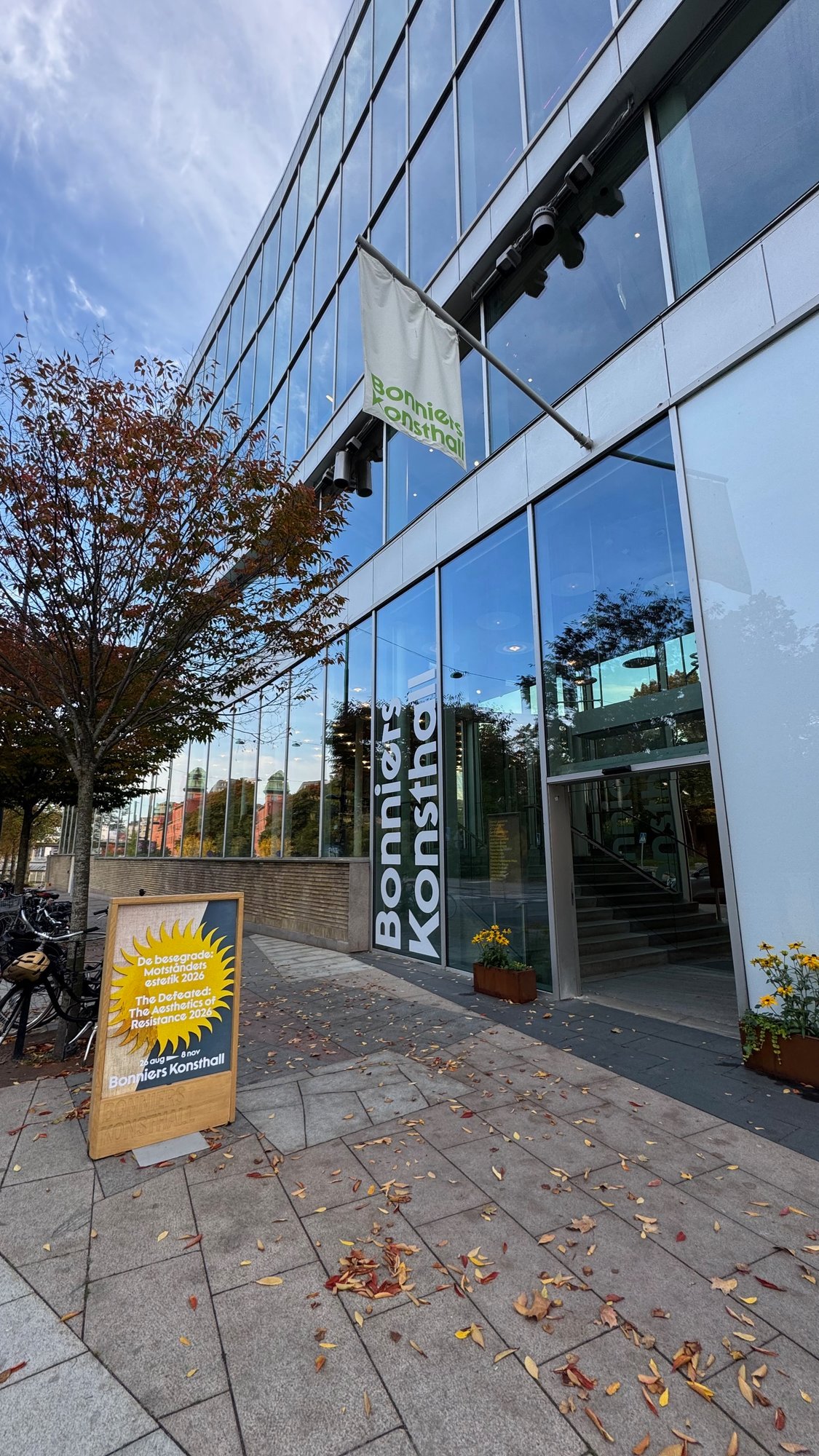 Entrance of Bonniers Konsthall with a green and white flag, the museum name on the glass, and a sign outside for the exhibition The Defeated: The Aesthetics of Resistance 2026.