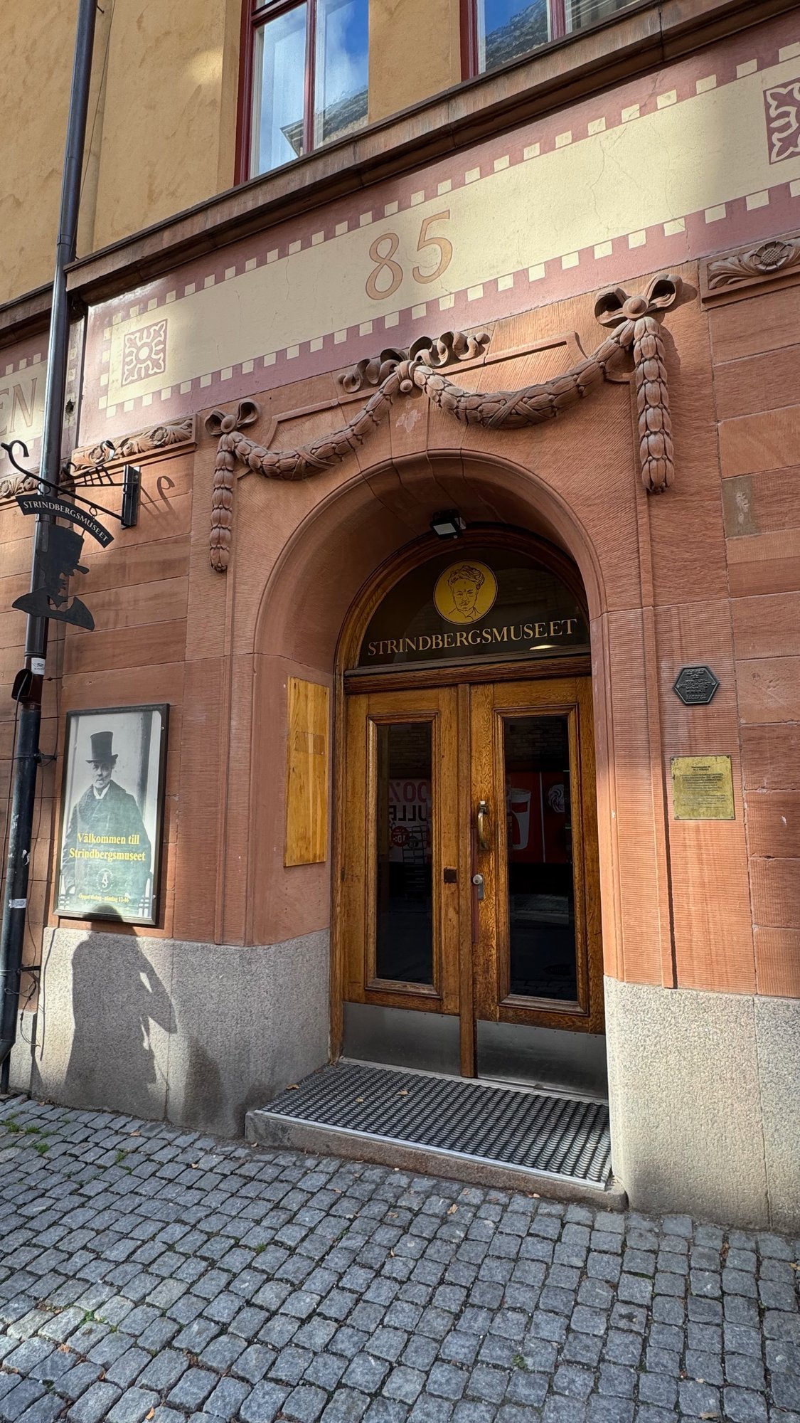 Arched stone entrance with a double wooden door and a decorated band above it, on the street.