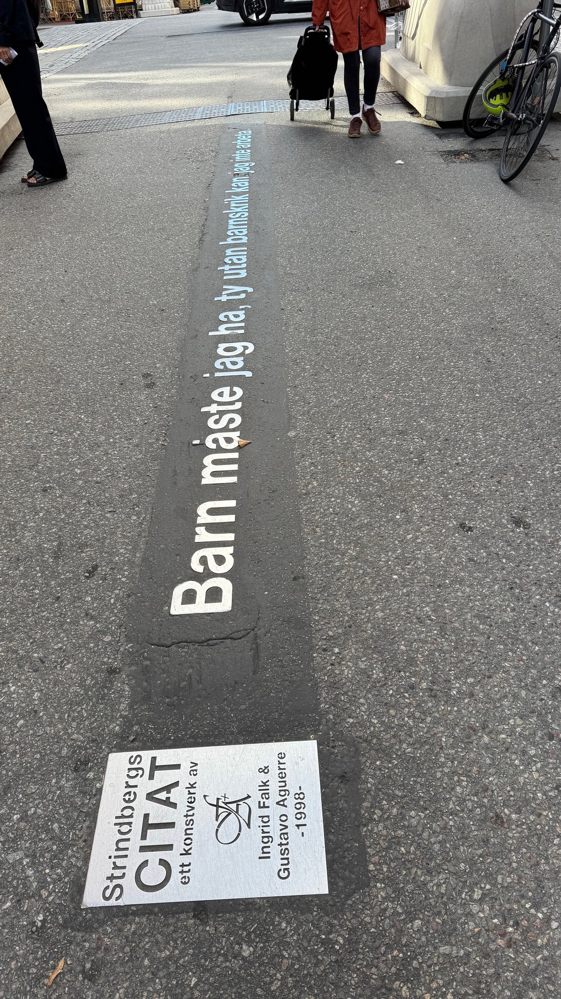 A Strindberg quote in white letters set into grey asphalt, with a small sign at the bottom.