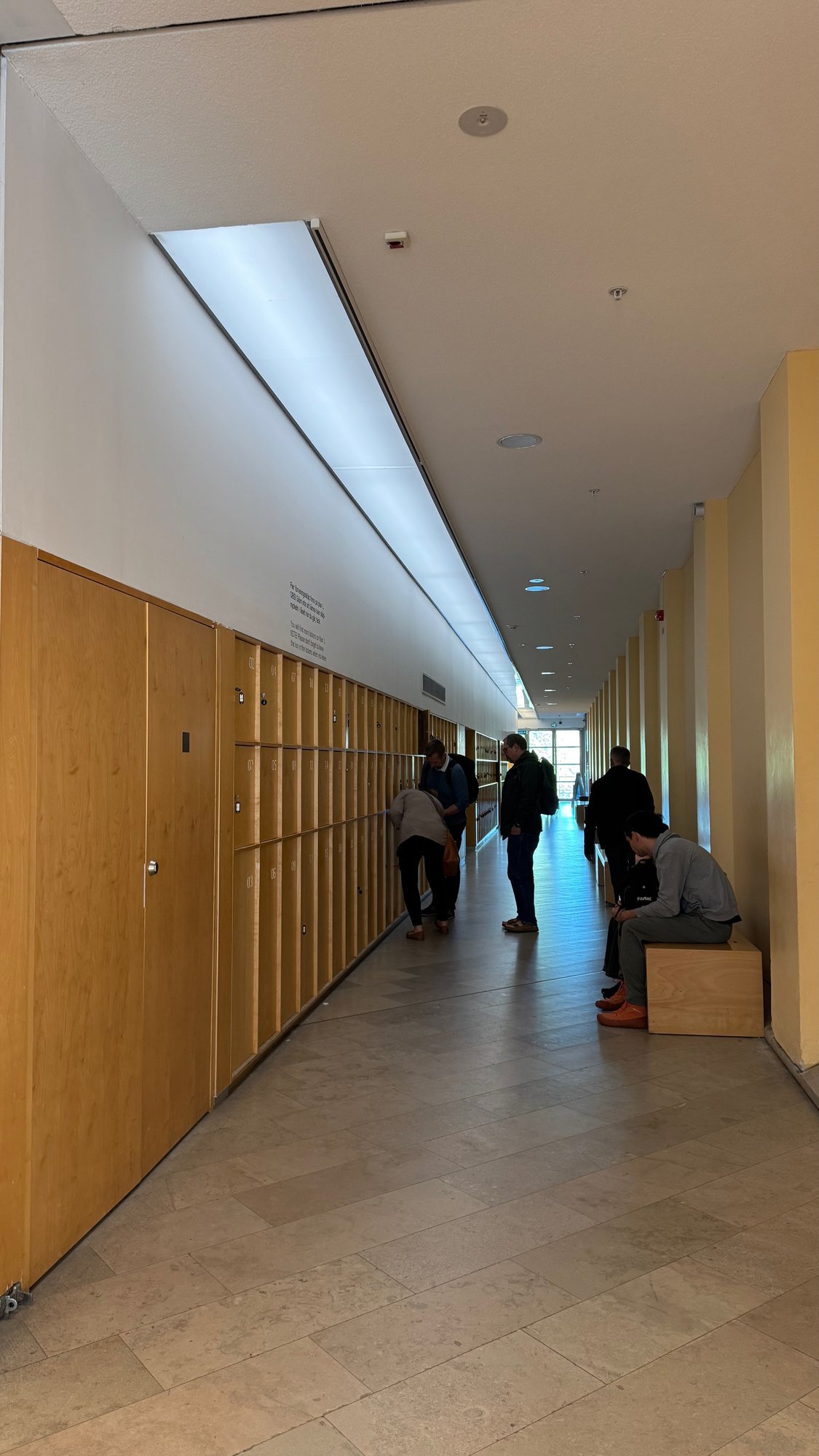 Long bright corridor with a wood-panelled wall on the left, a roof window and a few visitors.