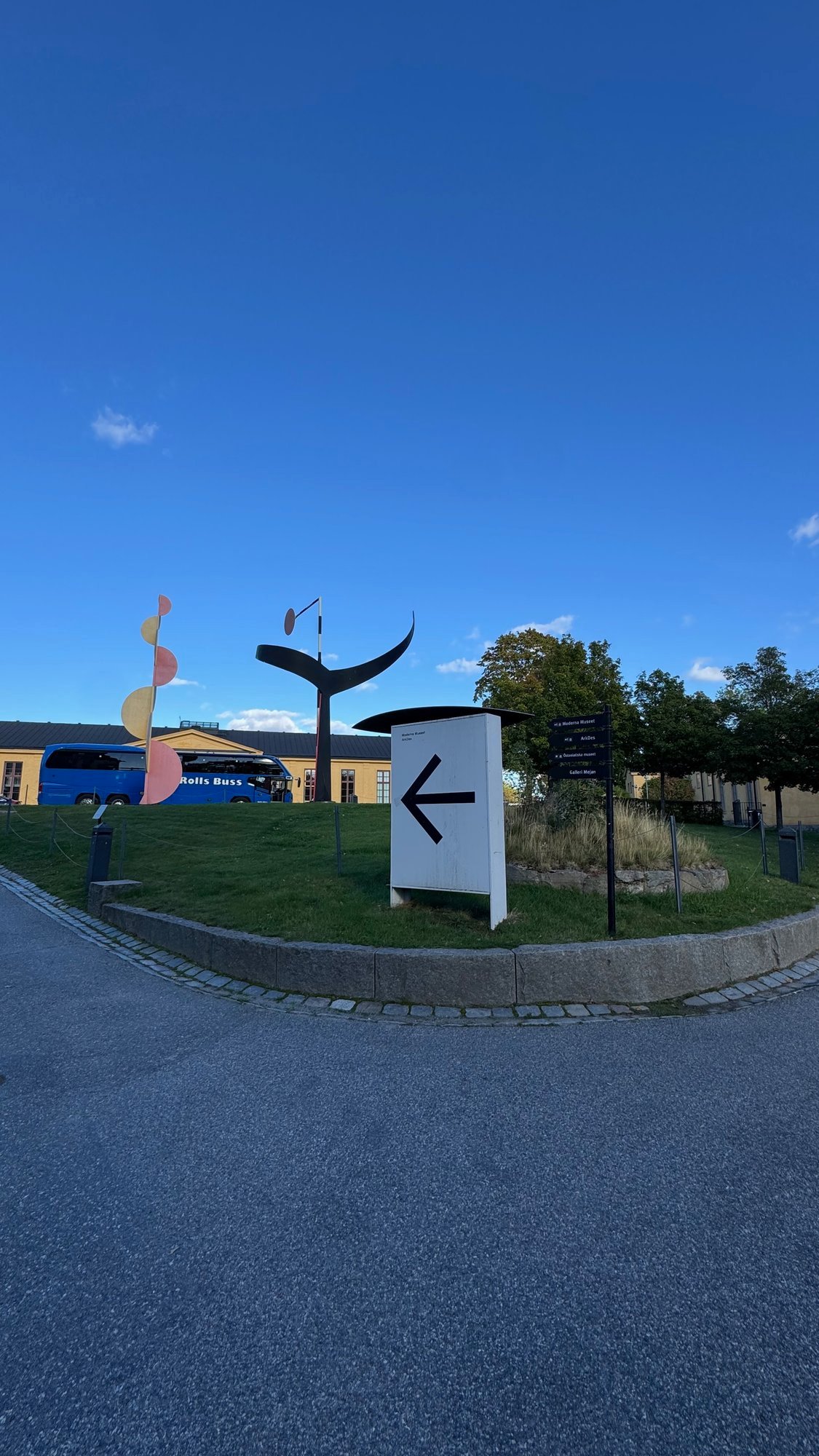 Wide-angle view of a lawn with colorful sculptures, a dark sculpture and a white sign with an arrow.