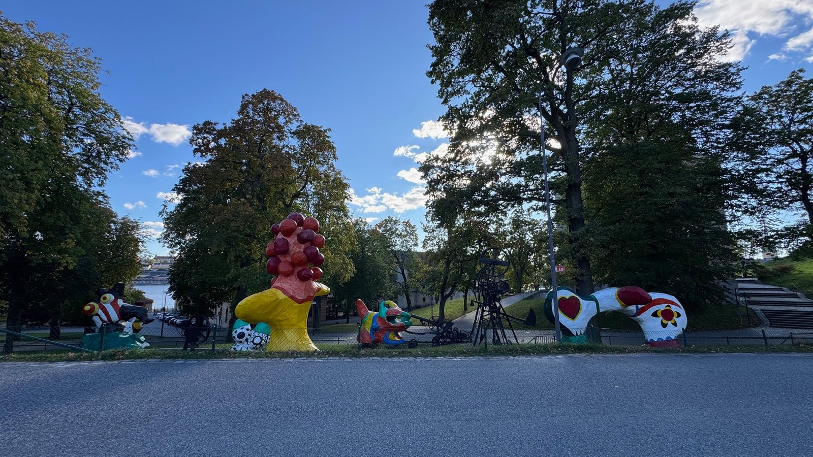 Colorful large sculptures on a lawn outside Moderna Museet, among tall trees under a blue sky.