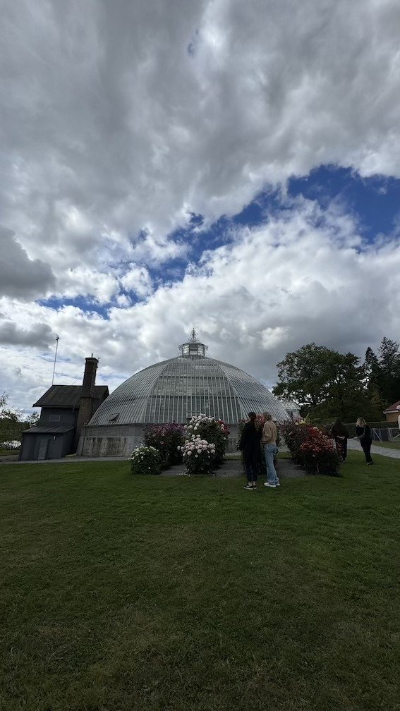 Round domed greenhouse building, the Victoria House, standing on a lawn with visitors walking nearby.