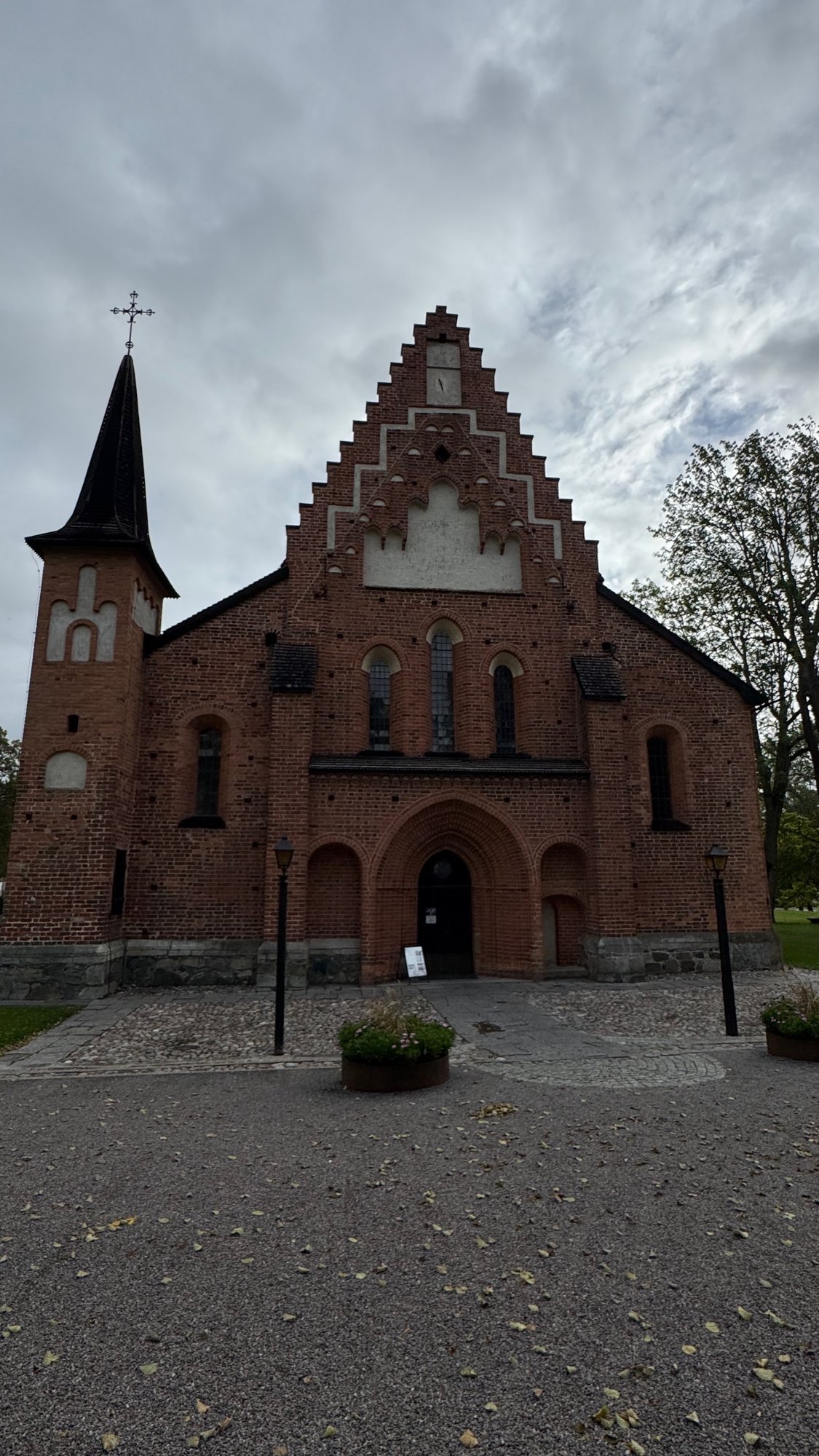 Red brick church with a stepped gable and a pointed arch window above a low entrance, seen from the churchyard under a blue sky.