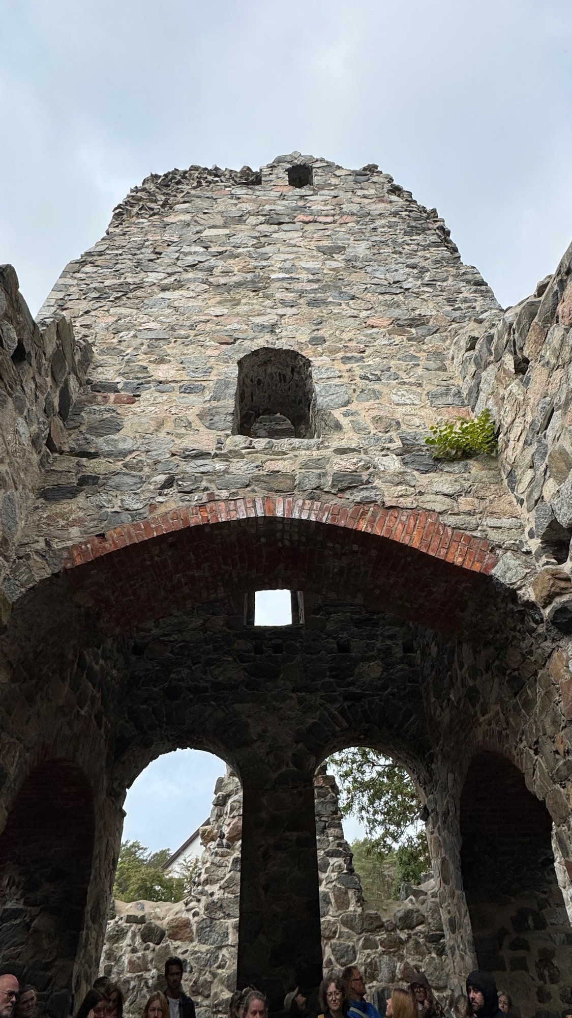 View upward inside a stone ruin, with a brick arch against the sky and rough stone walls.
