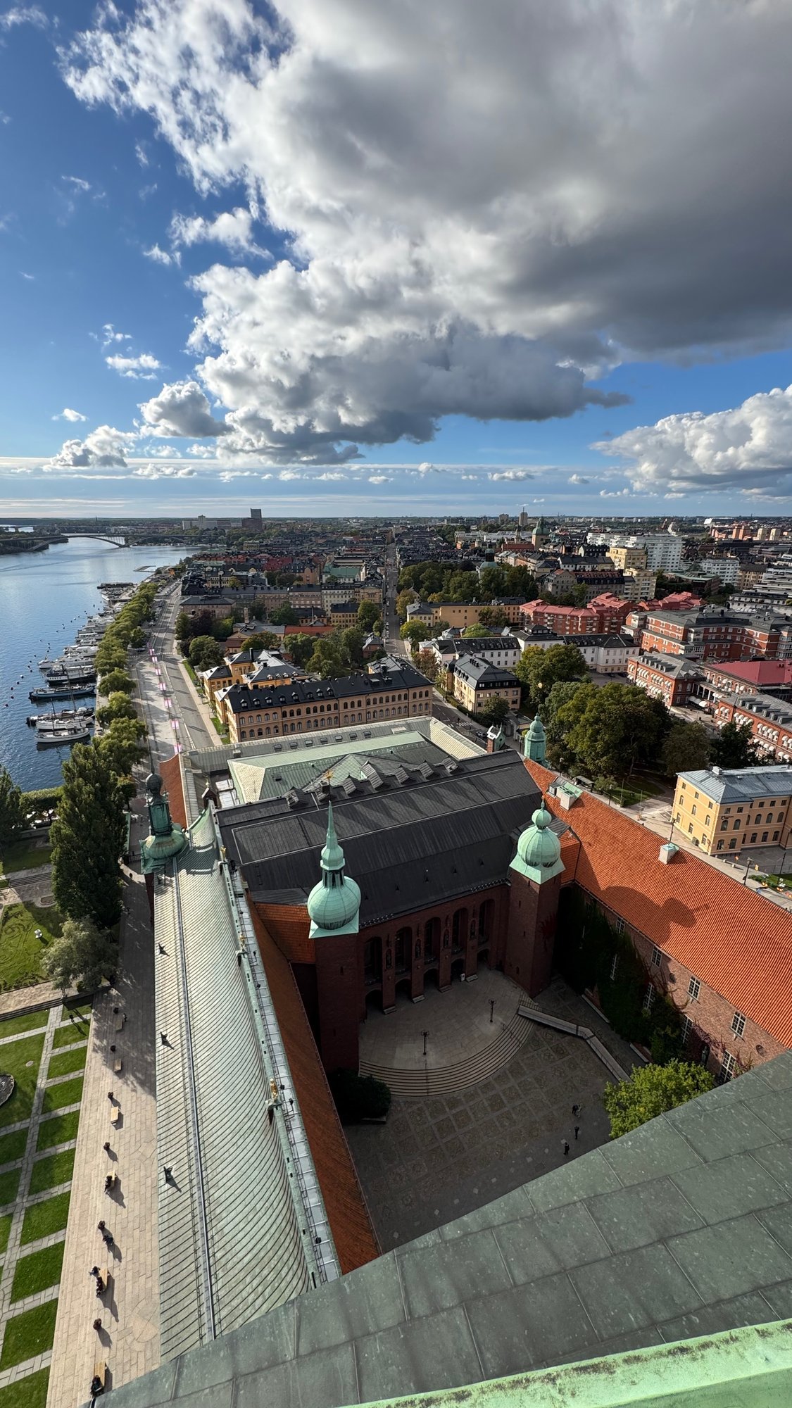 High view down at a brick courtyard with a paved square, red tile roofs, a green copper tower top and the water on the left.