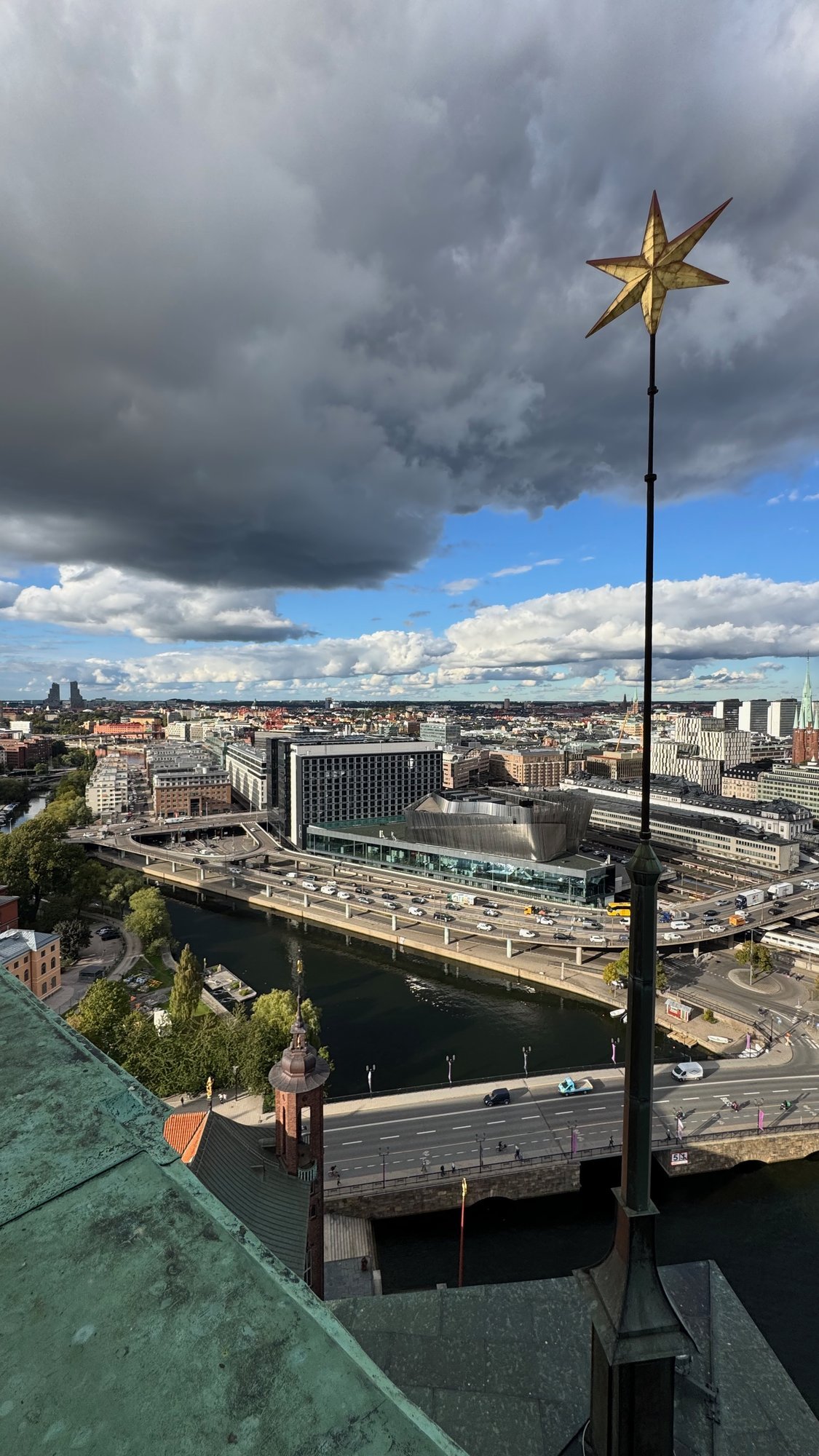 View to the east from the tower: a gold star on a tall pole, a bridge, roads and large buildings, with a heavy grey cloud above.