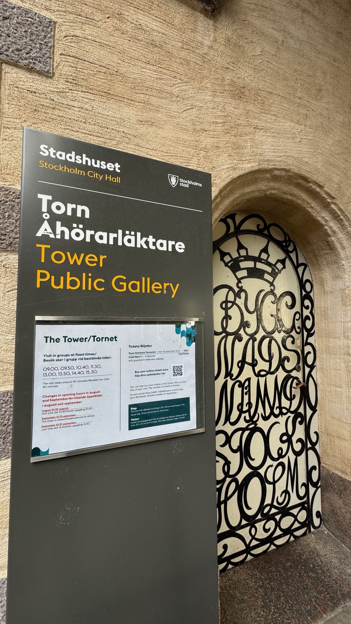 Dark sign on the stone wall that reads Torn, Åhörarläktare, Tower and Public Gallery, beside a black iron gate with curled lettering in front of an arched opening.