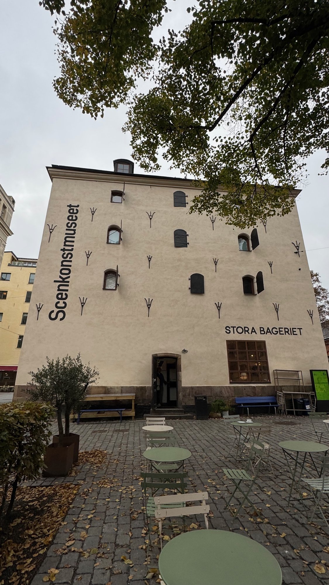 The white facade of Scenkonstmuseet with the sign Stora Bageriet and café tables in the courtyard, Stockholm.