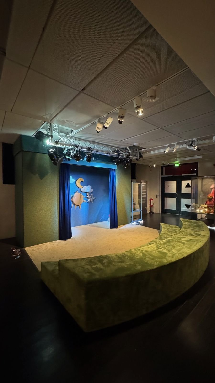 A small stage with a blue curtain and a long green bench at Scenkonstmuseet.