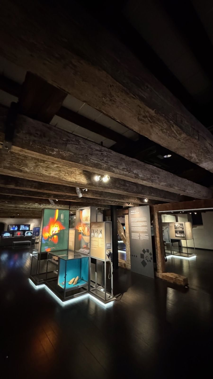 A dark exhibition hall with old wooden beams and lit displays at Scenkonstmuseet.