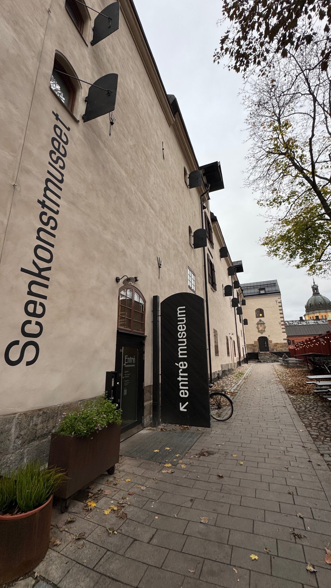 A paved lane along the Scenkonstmuseet building with a black sign entré museum.