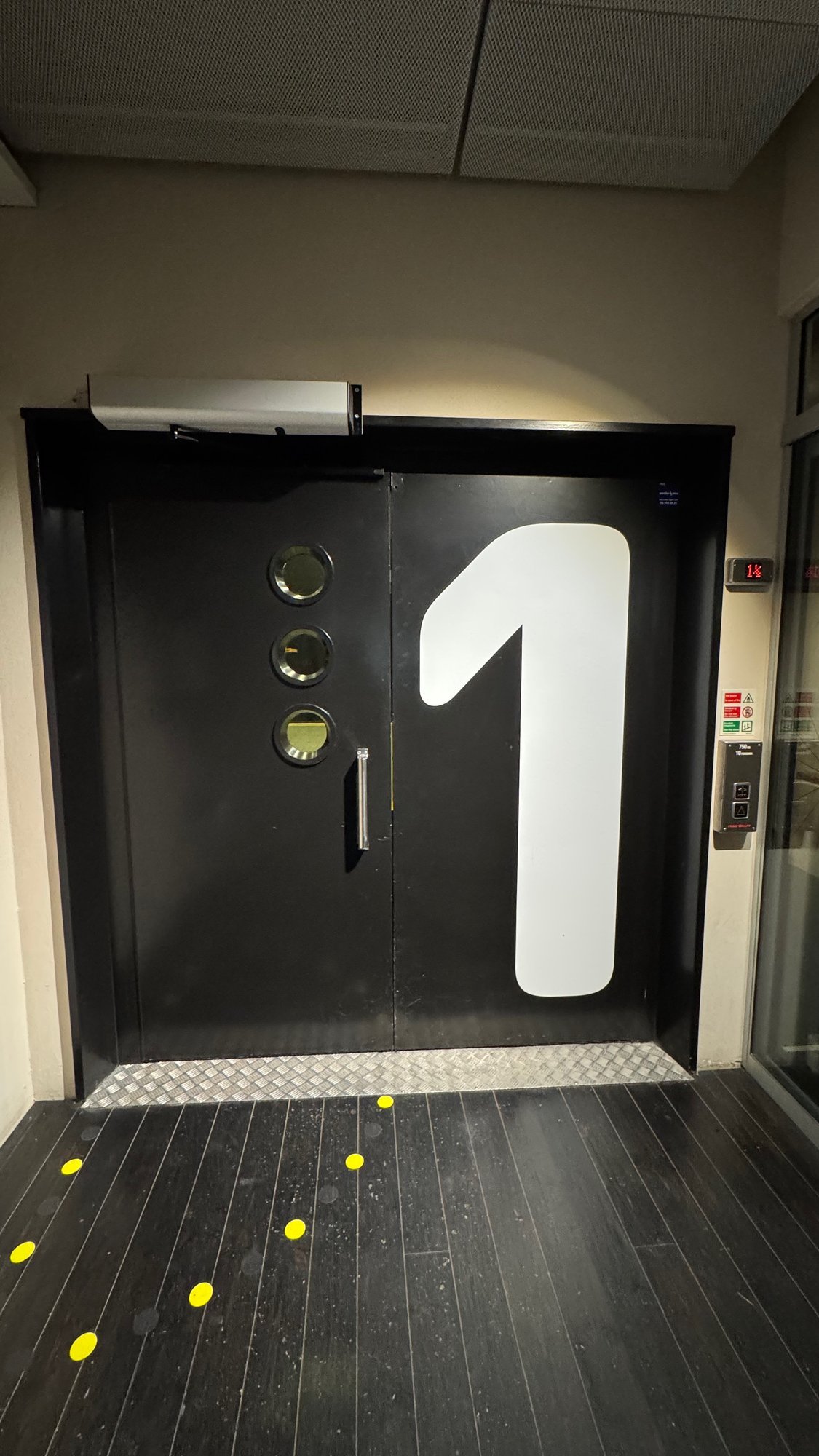 A black door with a large number 1 and yellow dots on the floor at Scenkonstmuseet.