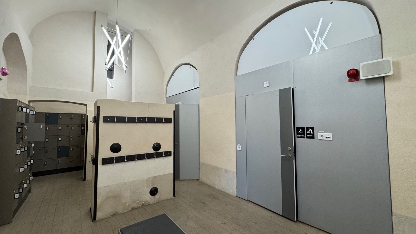 A cloakroom with grey lockers, a bench and large grey doors at Scenkonstmuseet.