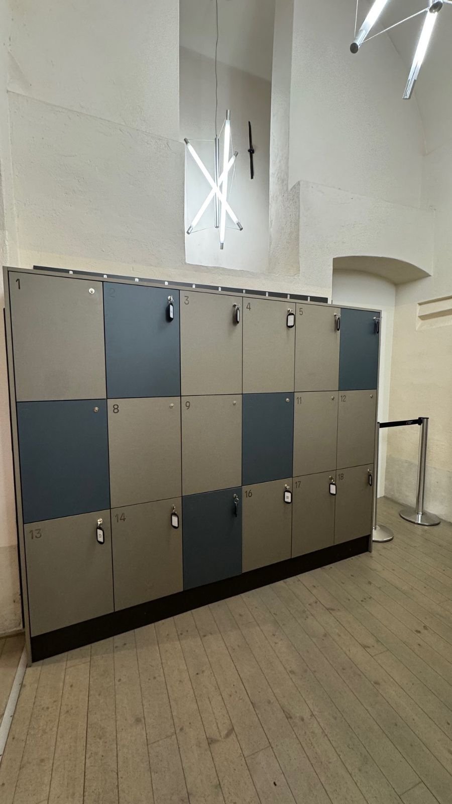 A wall of grey and blue lockers under a light sculpture at Scenkonstmuseet.