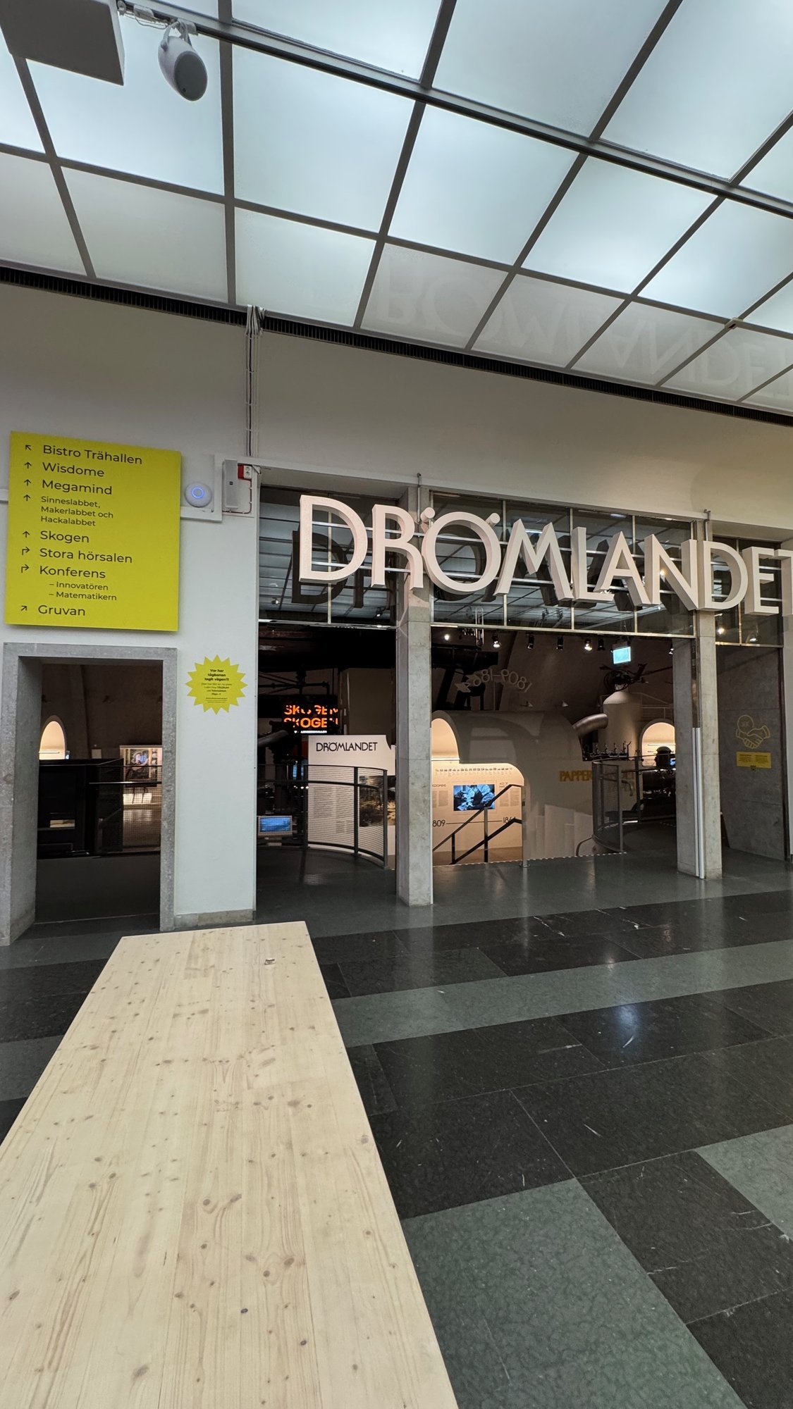 The entrance to the exhibition Drömlandet with large letters and a wooden bench at Tekniska museet.