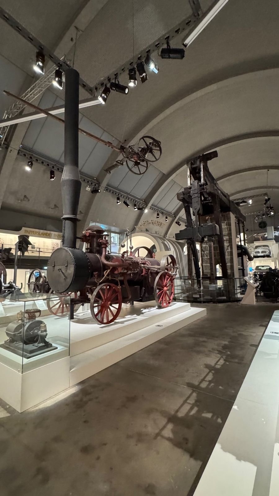 A red steam engine and old machines in the long machine hall at Tekniska museet.