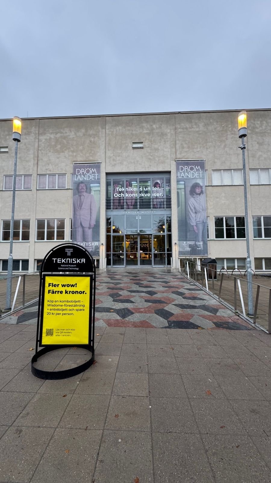 The main entrance of Tekniska museet in Stockholm with banners and a yellow sign on the stand outside.