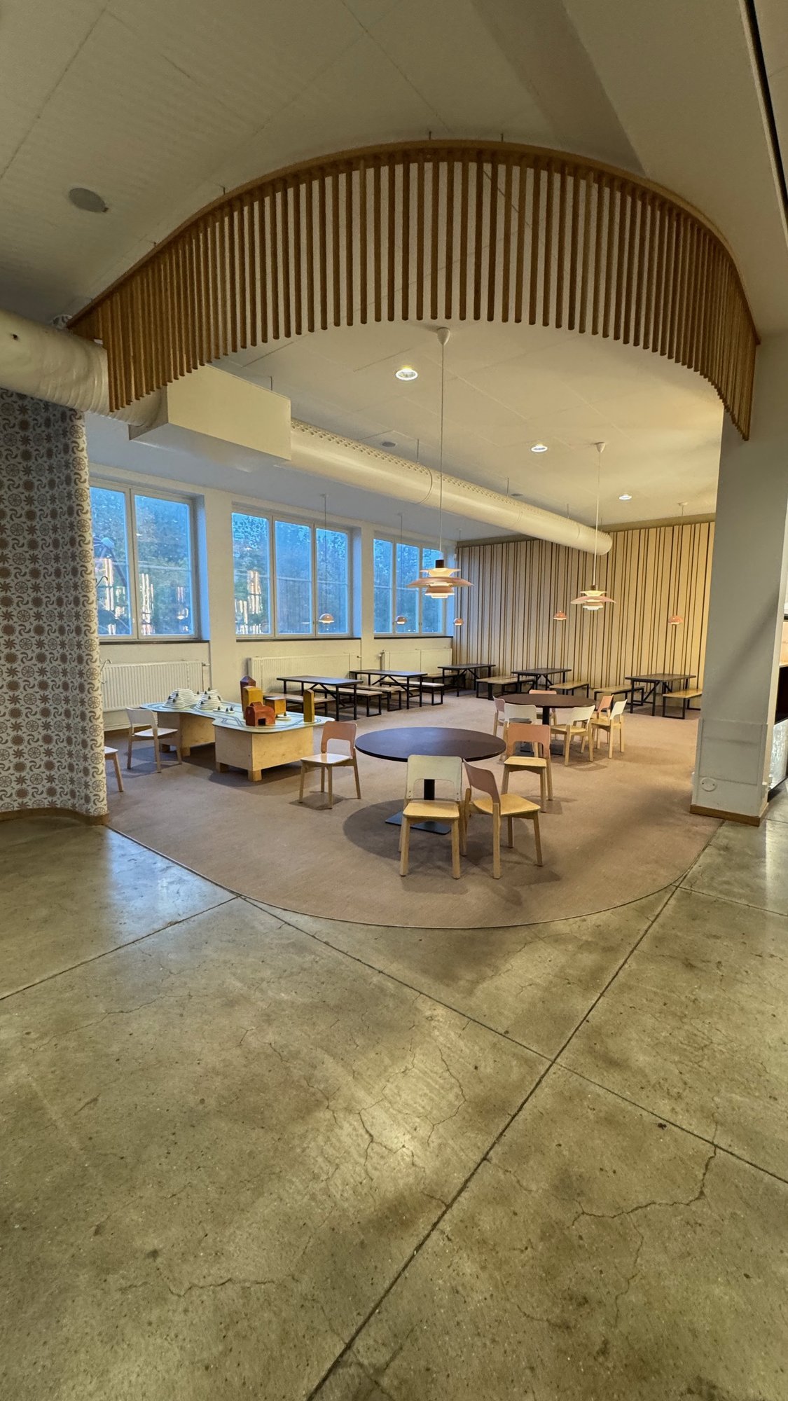 A hang-out area at Tekniska museet with round tables, small chairs, a wooden play table and a curved wooden arch by the windows.
