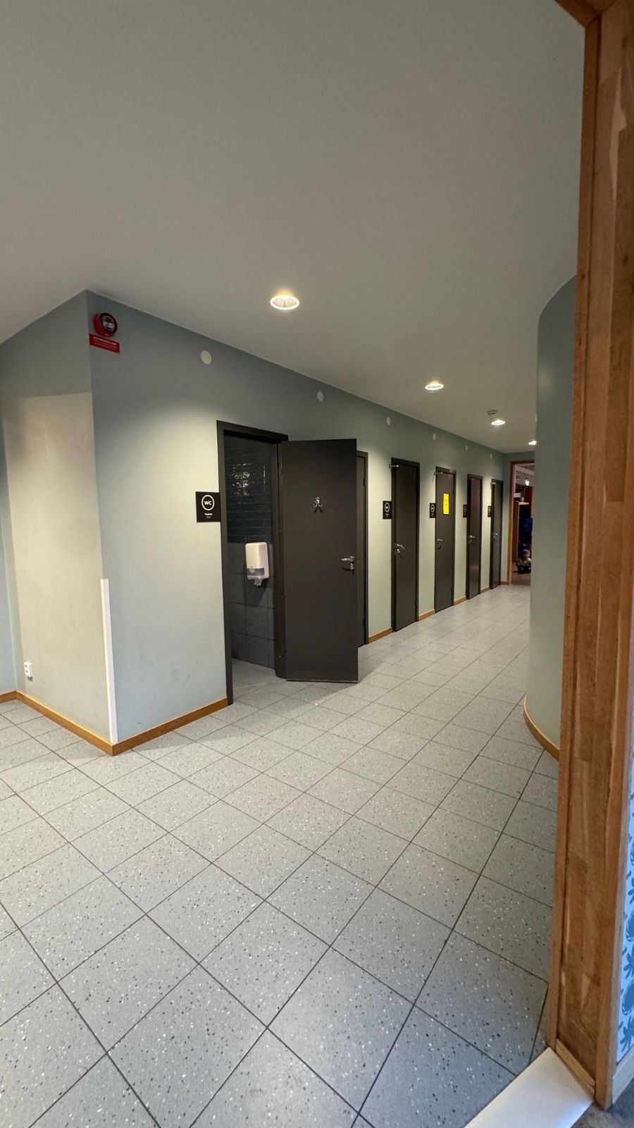 A bright corridor with toilet doors and a tiled floor at Tekniska museet.