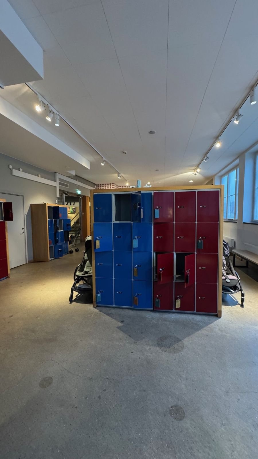 Blue and red lockers with strollers parked next to them in the entrance hall at Tekniska museet.