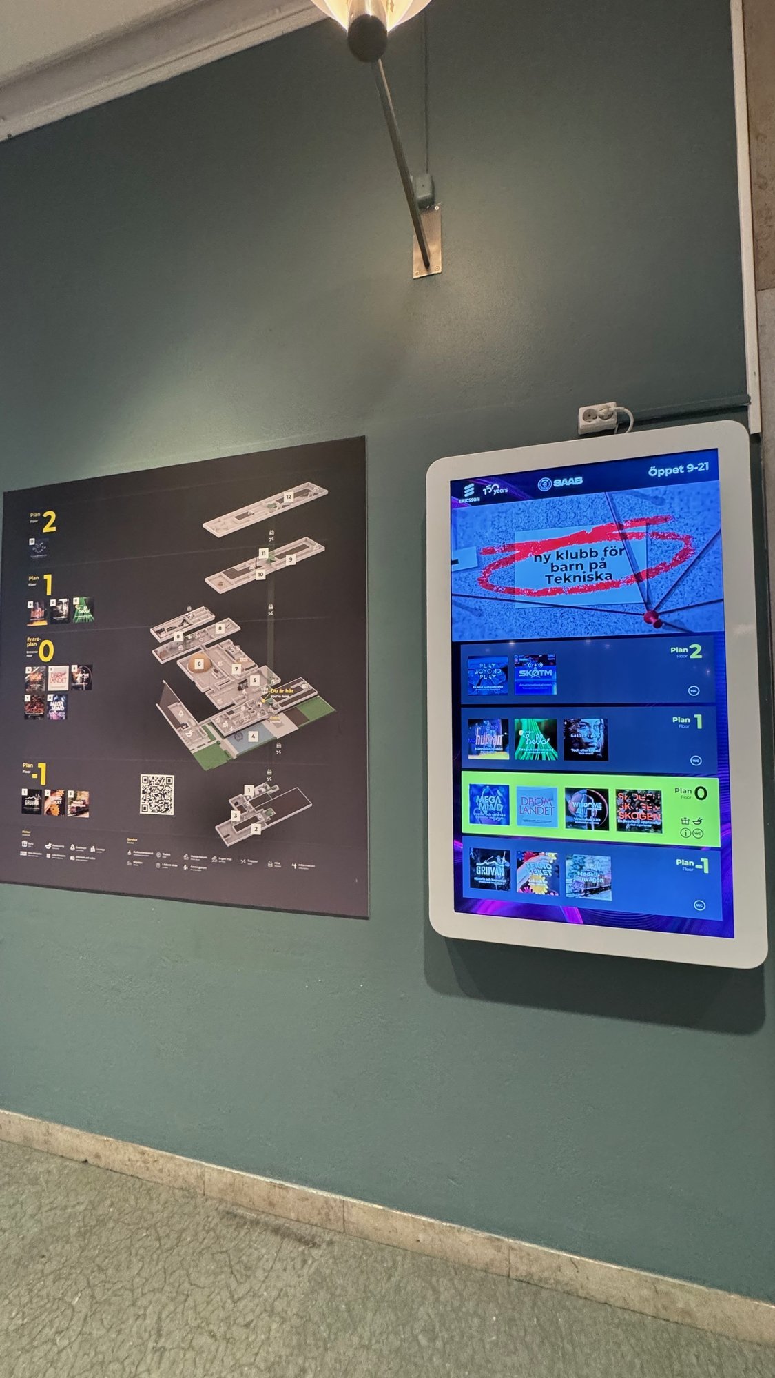 A floor map of the museum and a touch screen with exhibitions on a green wall at Tekniska museet.