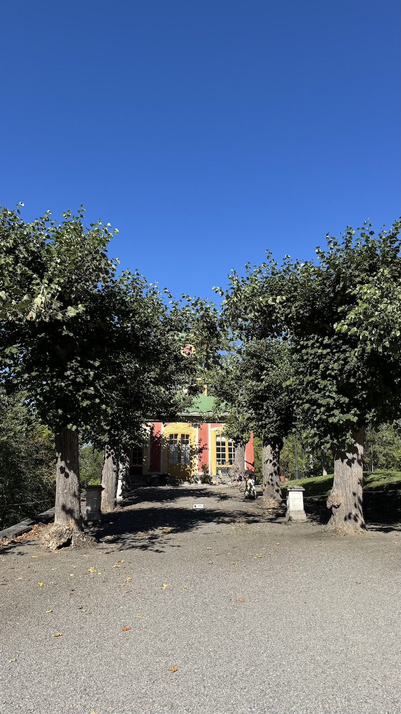 A gravel avenue lined with clipped trees, leading toward the yellow Chinese Pavilion in the distance.