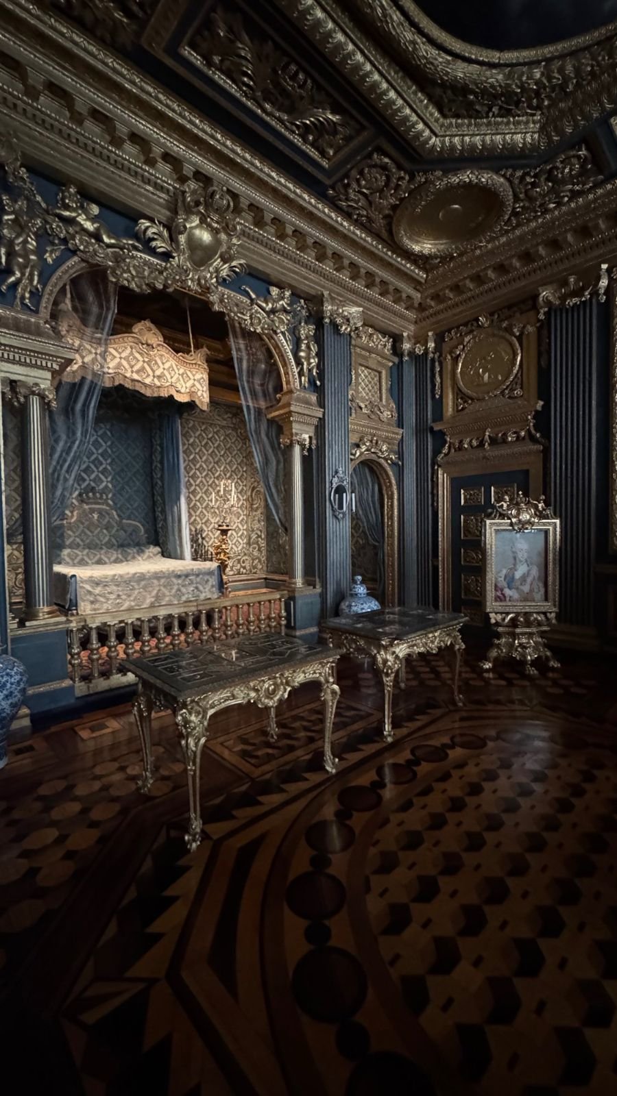 Hedvig Eleonora's State Bedchamber with a canopied bed in an alcove, dark blue and gold walls and a patterned parquet floor.