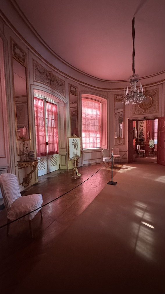 A curved palace room at Drottningholm, decorated in red and gold, with tall windows and a crystal chandelier.