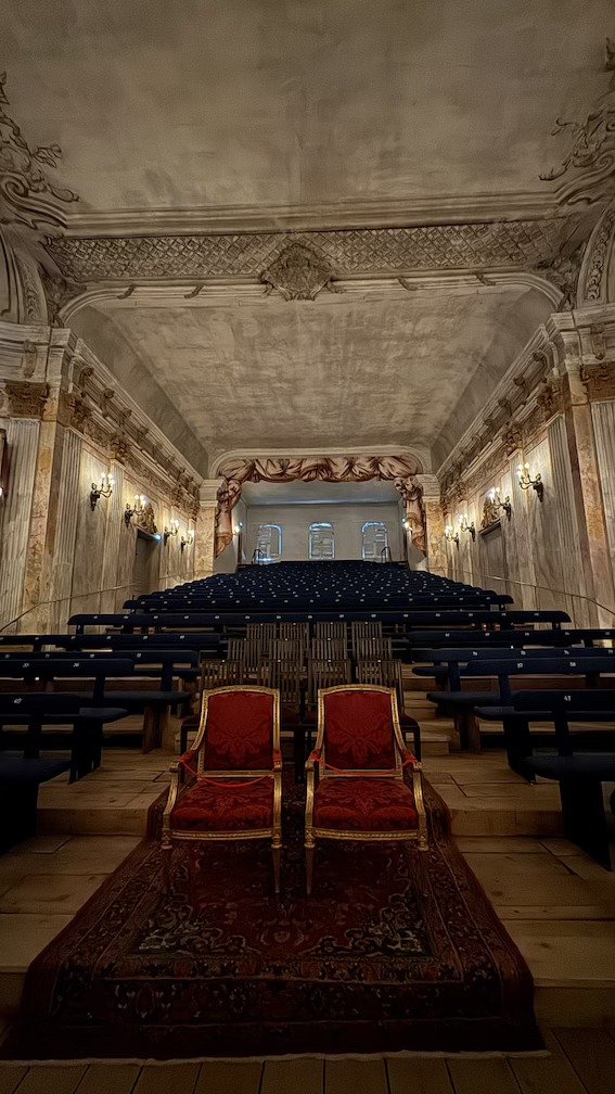 Two red upholstered chairs standing on a patterned carpet in the aisle of Drottningholm Palace Theatre, one of the world's oldest theatres still using its original stage machinery.