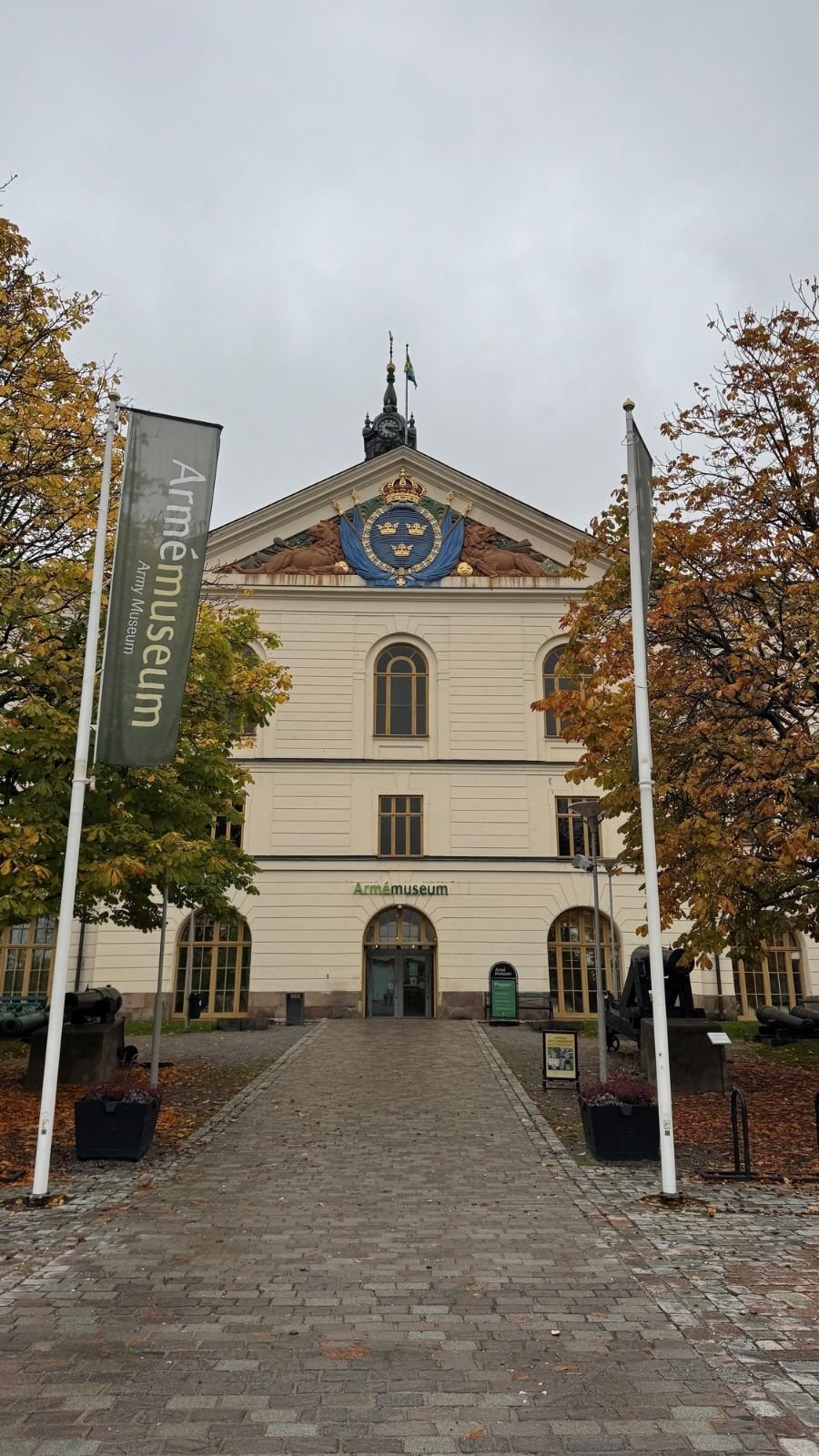 The yellow facade of Armémuseum in Stockholm with a green banner and a stone path to the entrance.