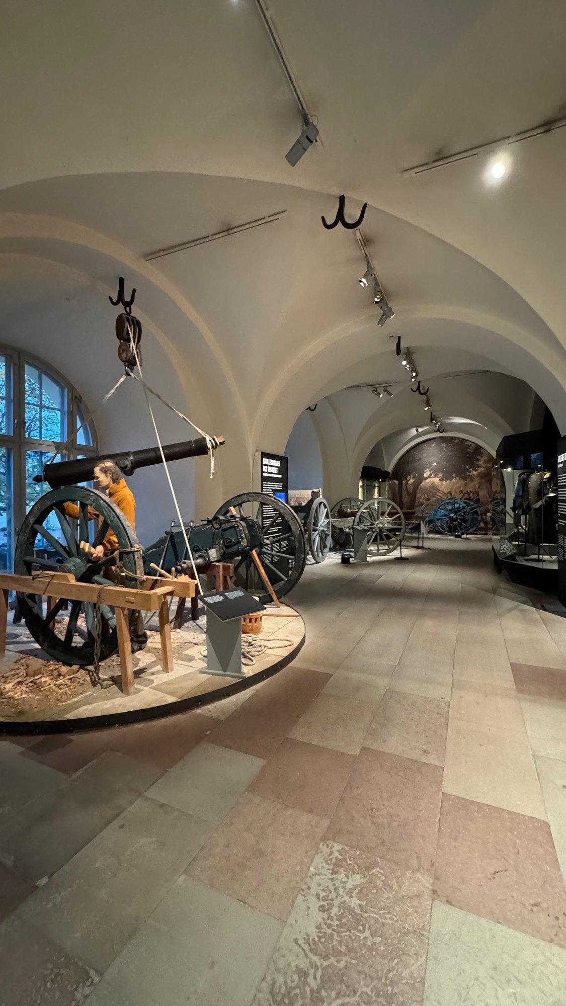 Old cannons and a soldier figure stand in a long hall with white vaults at Armémuseum.
