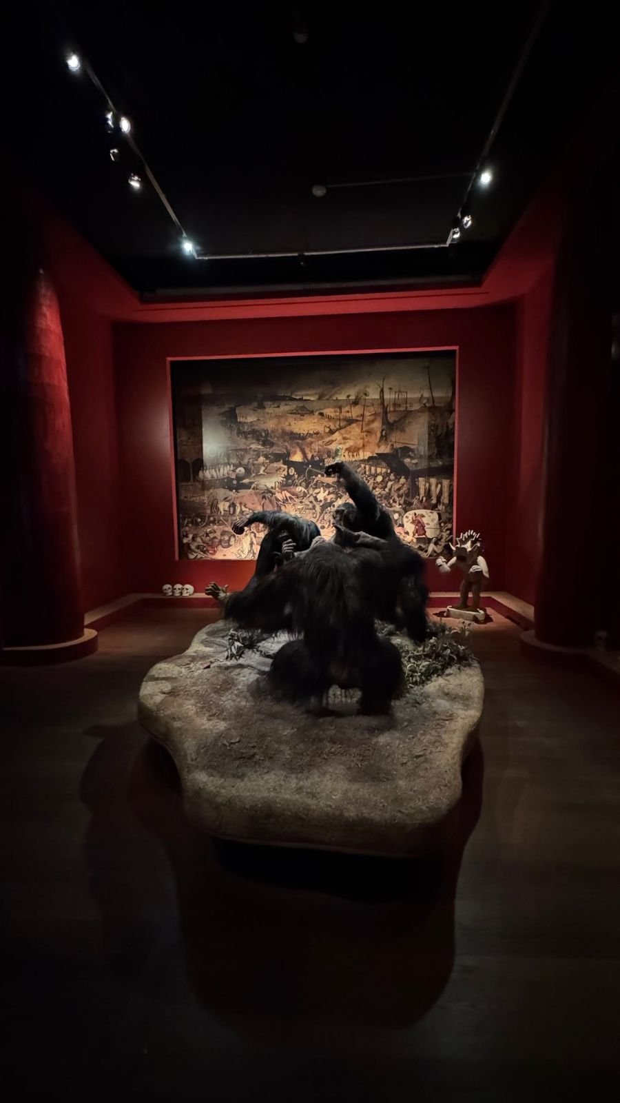 A diorama of fighting chimpanzees on a rock in front of a large painting of a battlefield in a red room at Armémuseum.