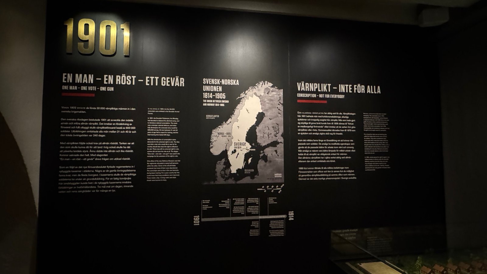 A dark exhibition wall with the year 1901 and texts about conscription and the union with Norway at Armémuseum.