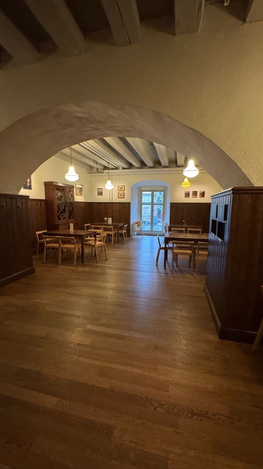 A café room with wooden tables, chairs and lamps under white arches at Armémuseum.