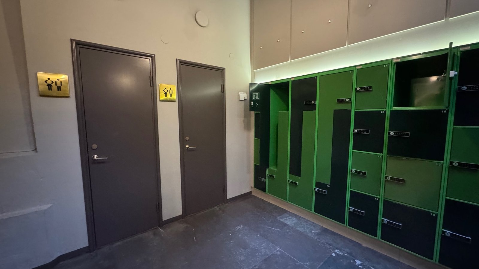 Two toilet doors with signs and a wall of green lockers in a corridor at Armémuseum.