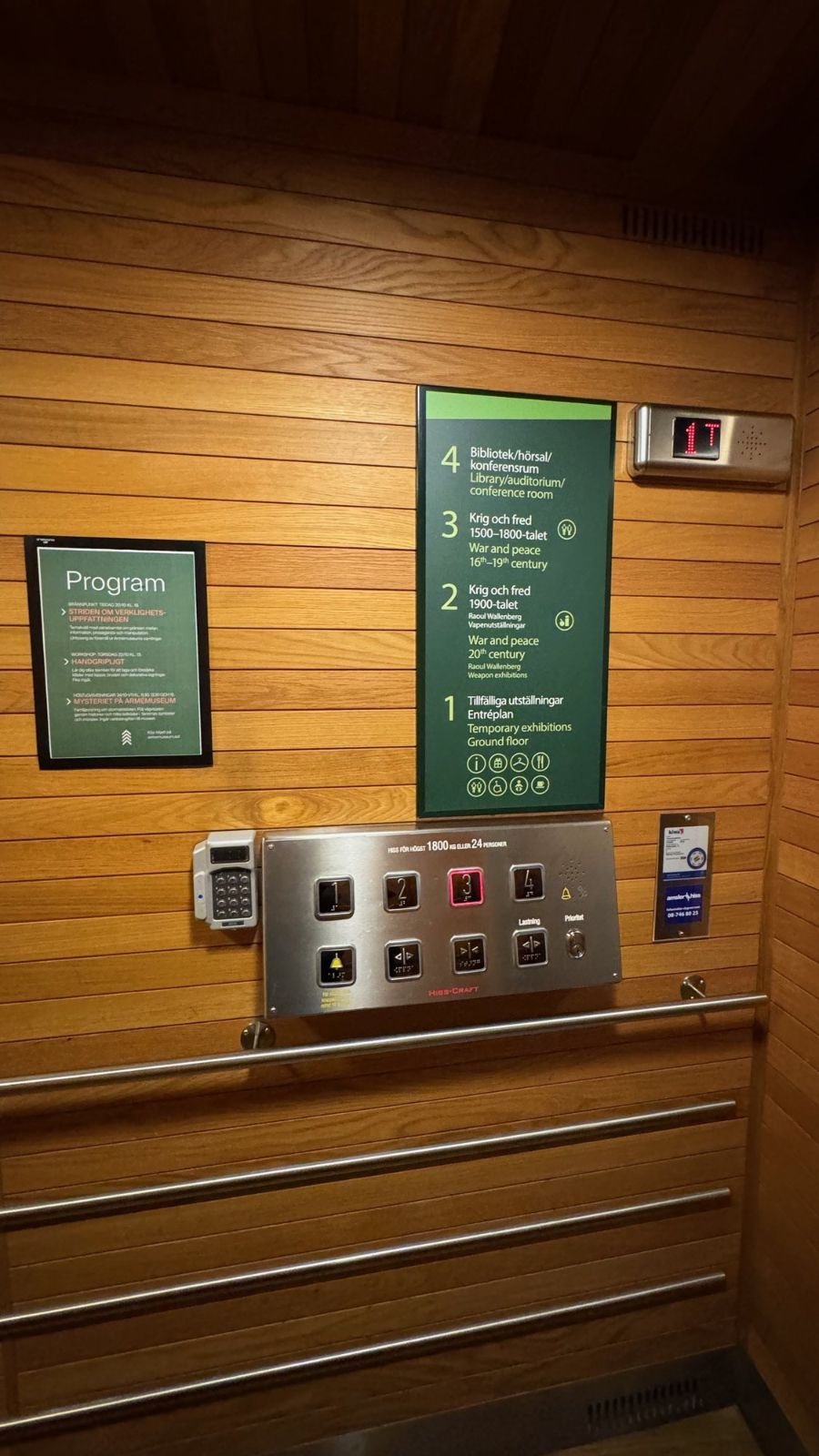 The inside of a lift with wooden walls, a floor guide for four floors and a button panel at Armémuseum.