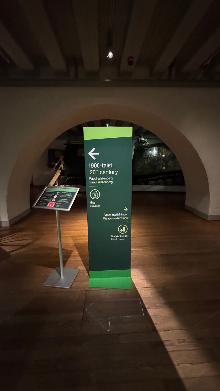 A green direction sign below an arch points to the 20th century exhibition, the lift and the picnic room at Armémuseum.