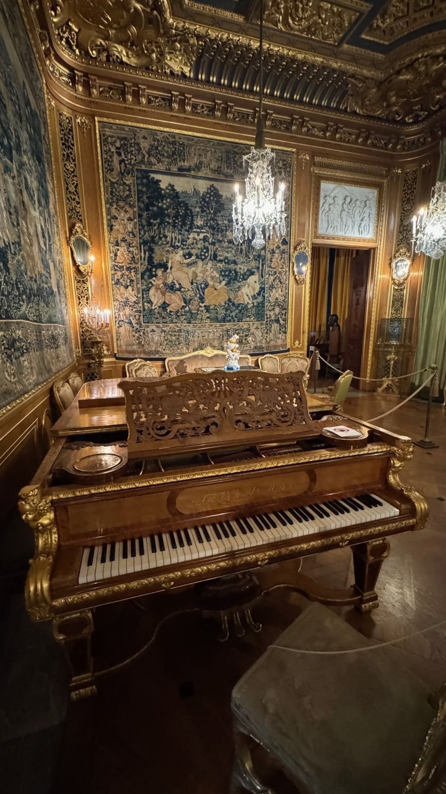 A carved grand piano in front of a large tapestry in the great salon of the Hallwyl Museum.