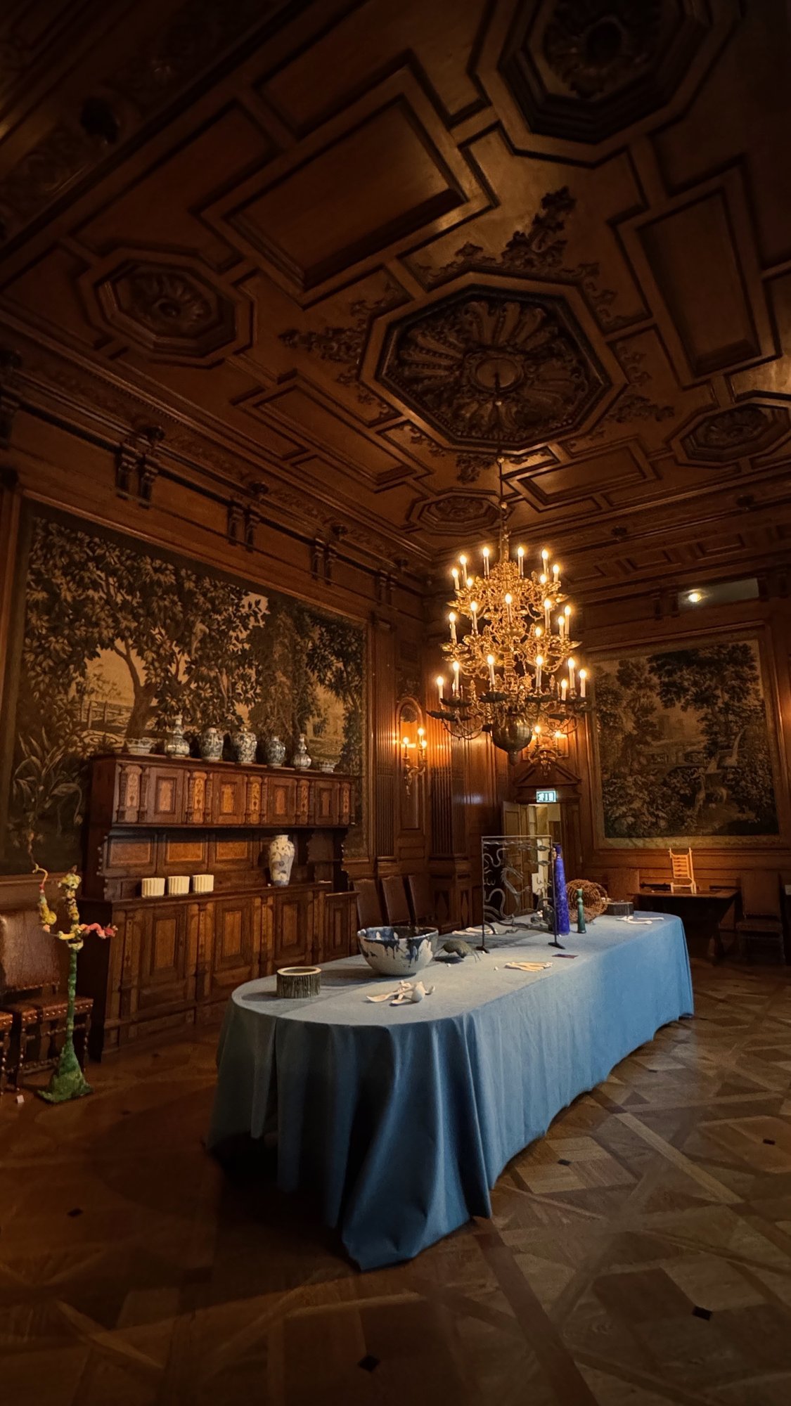 A dining room with a long table, a blue tablecloth, a chandelier and a carved ceiling at the Hallwyl Museum.