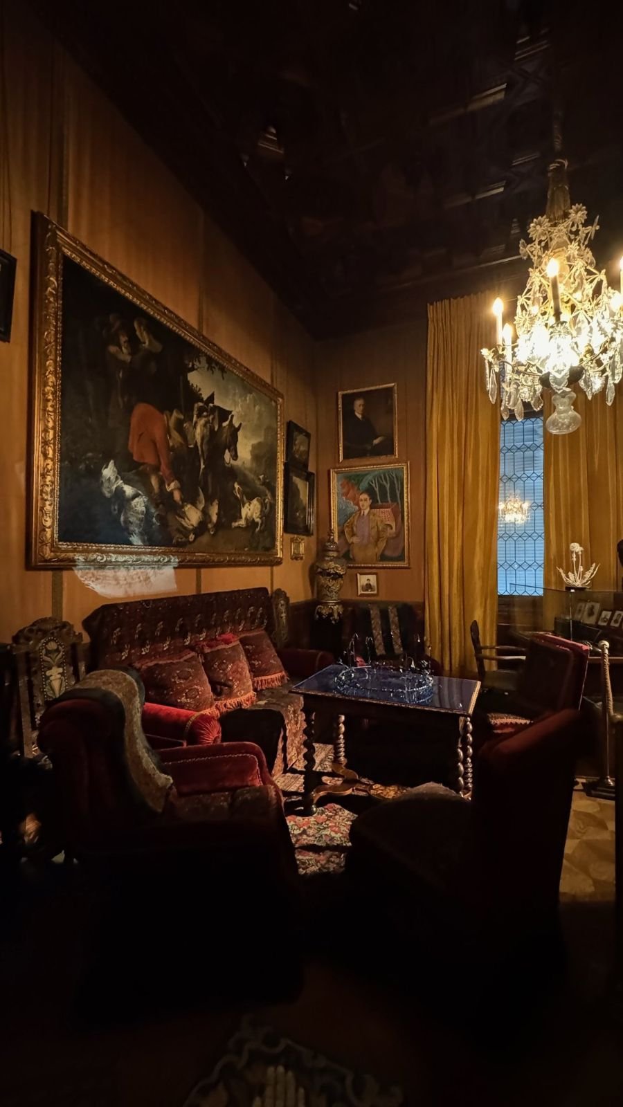 A dark room with red sofas, a crystal chandelier and large paintings at the Hallwyl Museum.