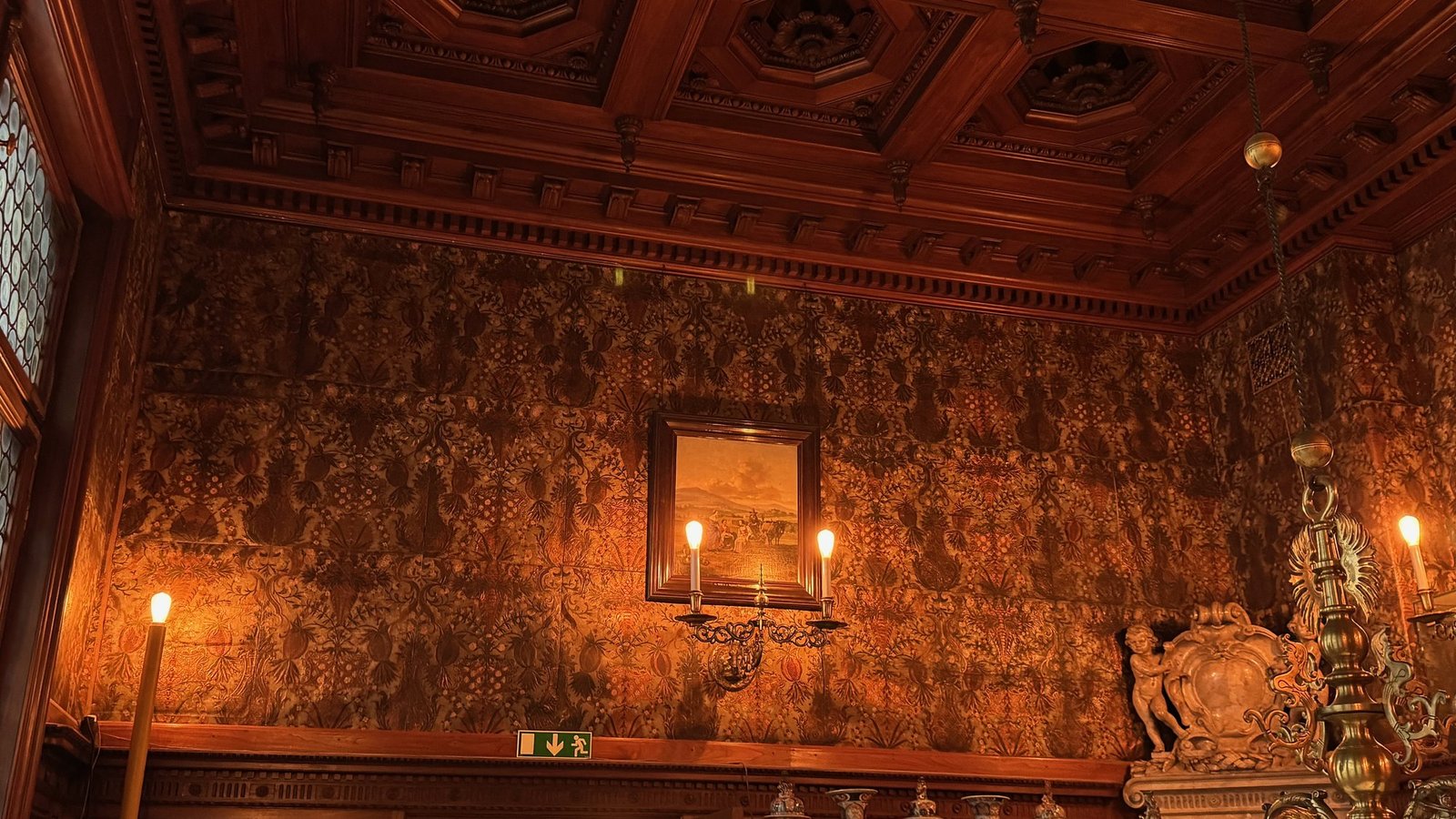 A room with gold patterned walls, a coffered ceiling and candle lights at the Hallwyl Museum.