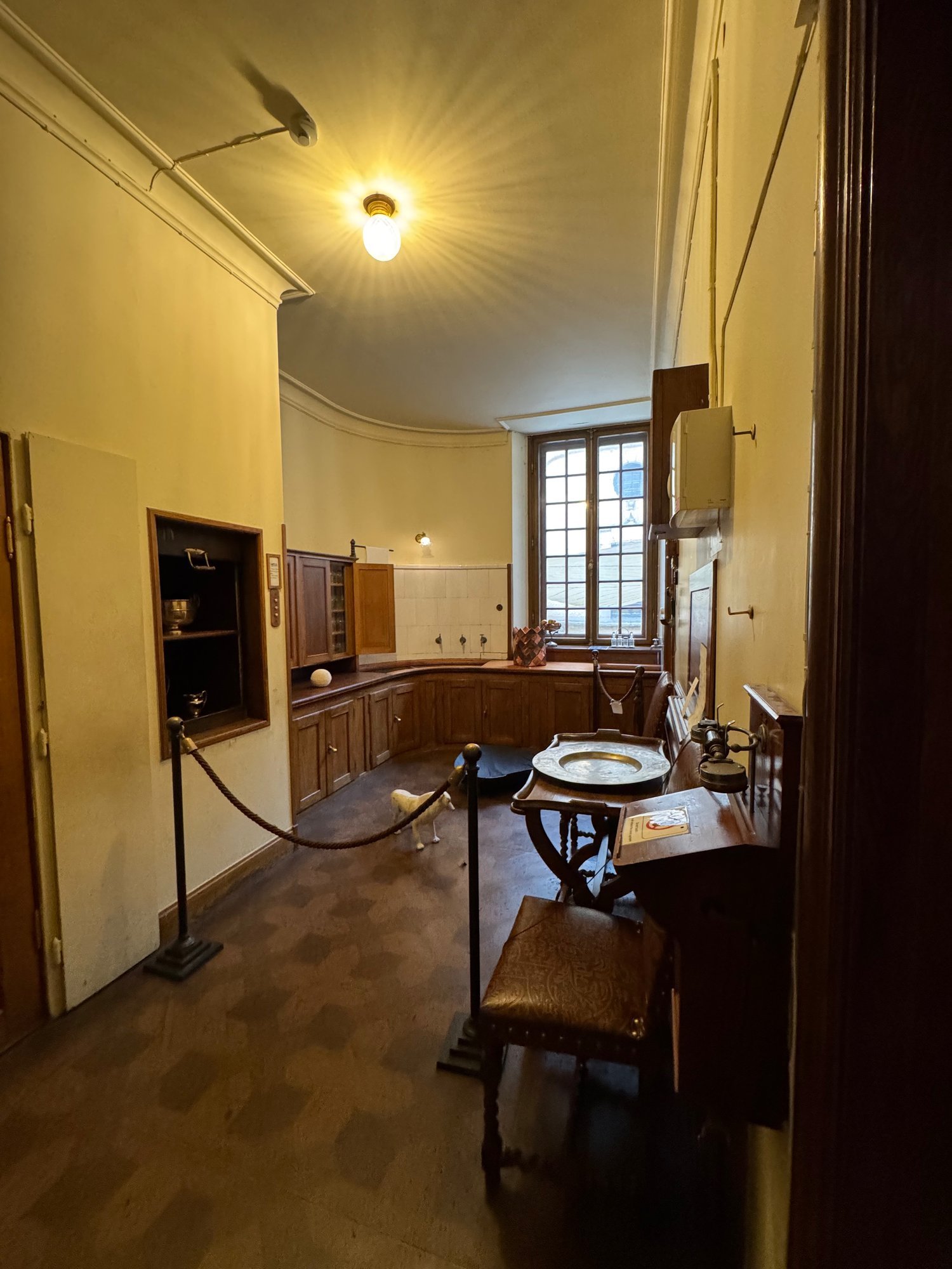 A service room in the Hallwyl house with wooden cupboards, a window, a washbasin and a rope barrier.