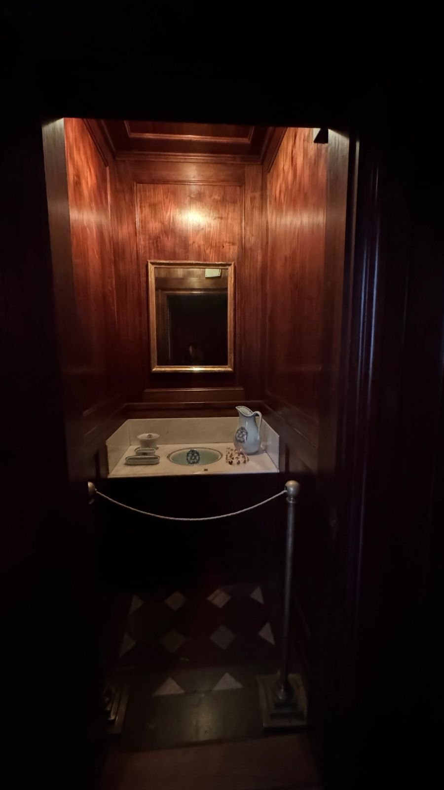 A small bathroom with dark wood walls, a mirror and a marble washstand at the Hallwyl Museum.
