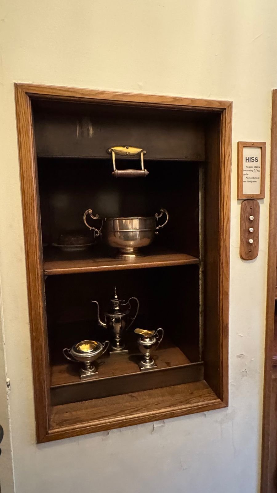 A food lift in the wall with a silver dish and a bowl, used to send warm food up to the dining room at the Hallwyl Museum.
