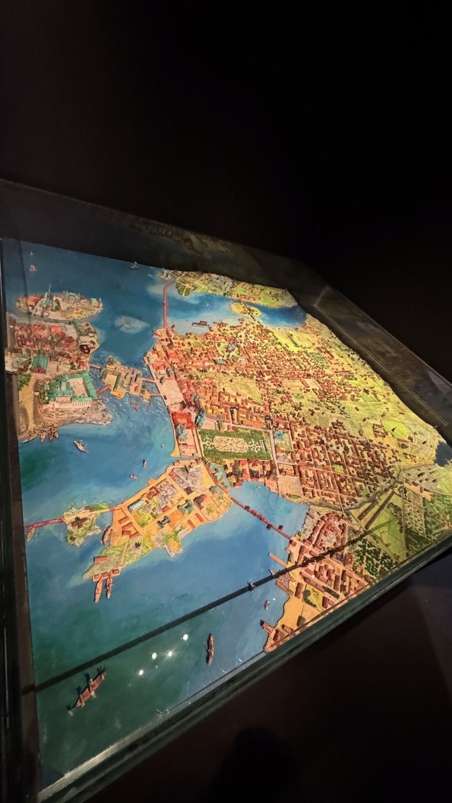 A colorful painted model of Stockholm city lies in a dark glass case at the Stockholm City Museum.