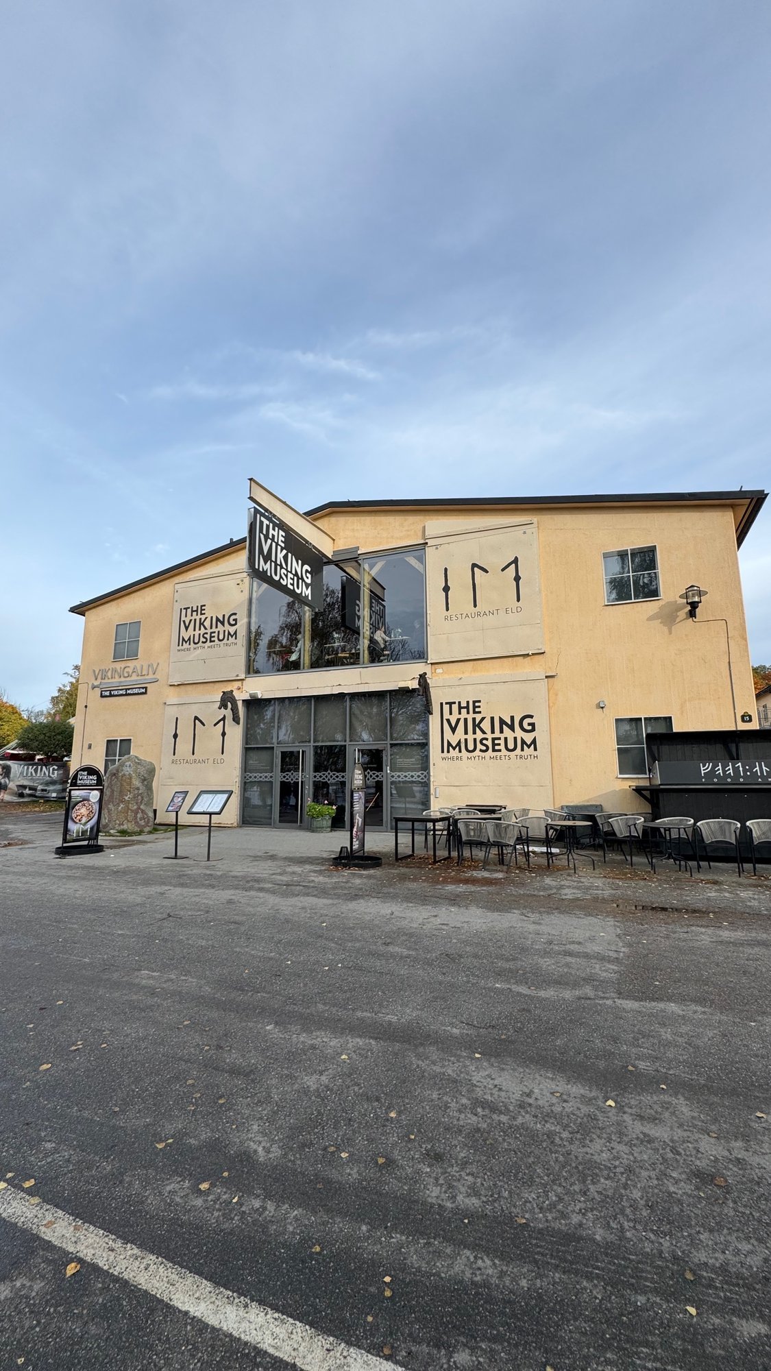 The yellow building of The Viking Museum on Djurgården, with black signs and an outdoor terrace.