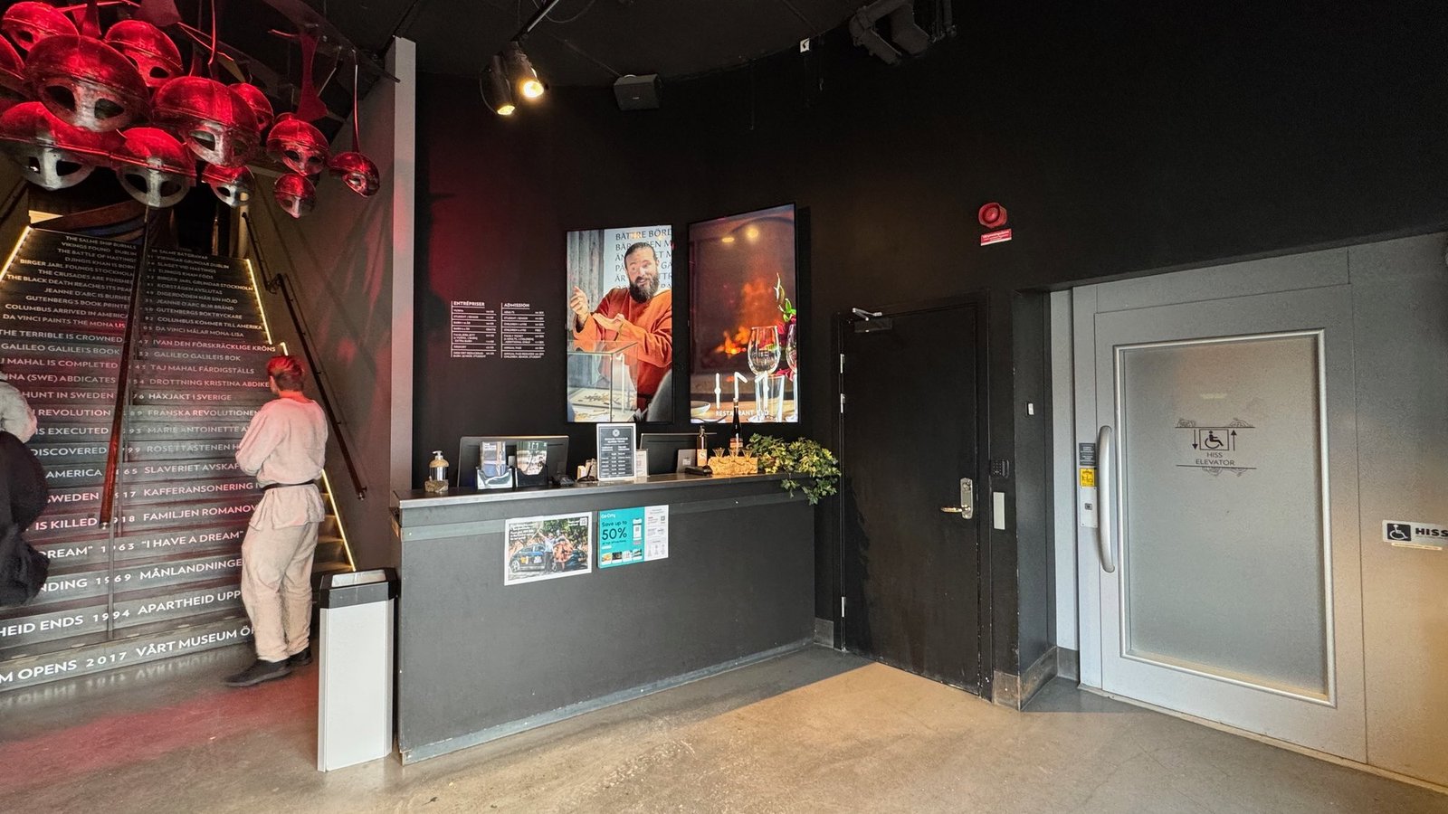 The ticket desk at The Viking Museum, with red helmets above the stairs and a lift door with a wheelchair sign.