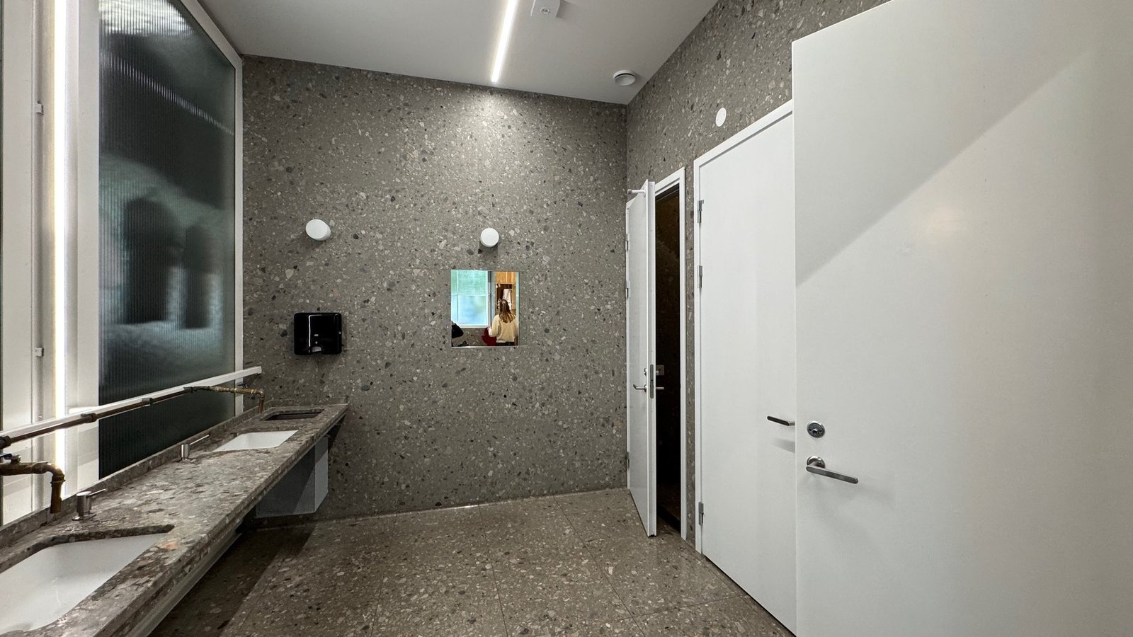A clean restroom at Vrak Museum of Wrecks with a long stone sink counter, grey walls and toilet doors.