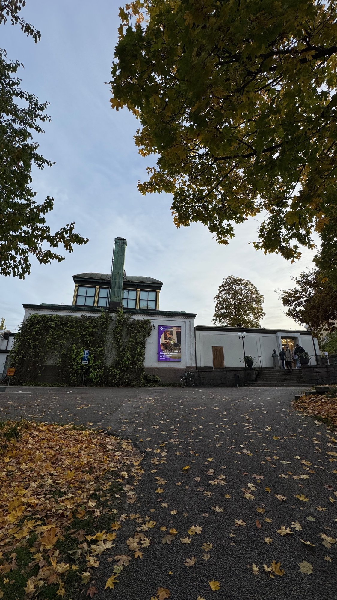 A path covered with yellow leaves leads to the white gallery building at Waldemarsudde.